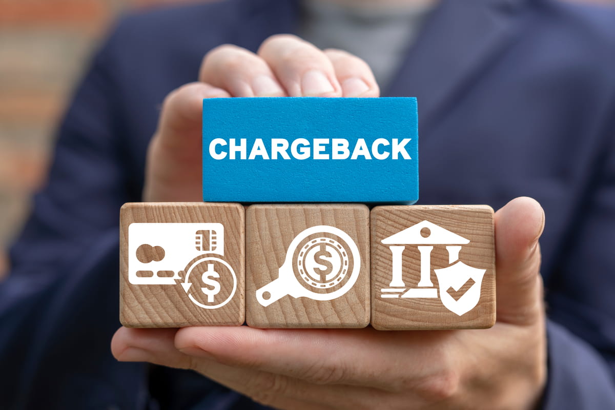 Hände, die Holzklötze mit der Aufschrift „CHARGEBACK“ und Symbolen für Finanztransaktionen halten.