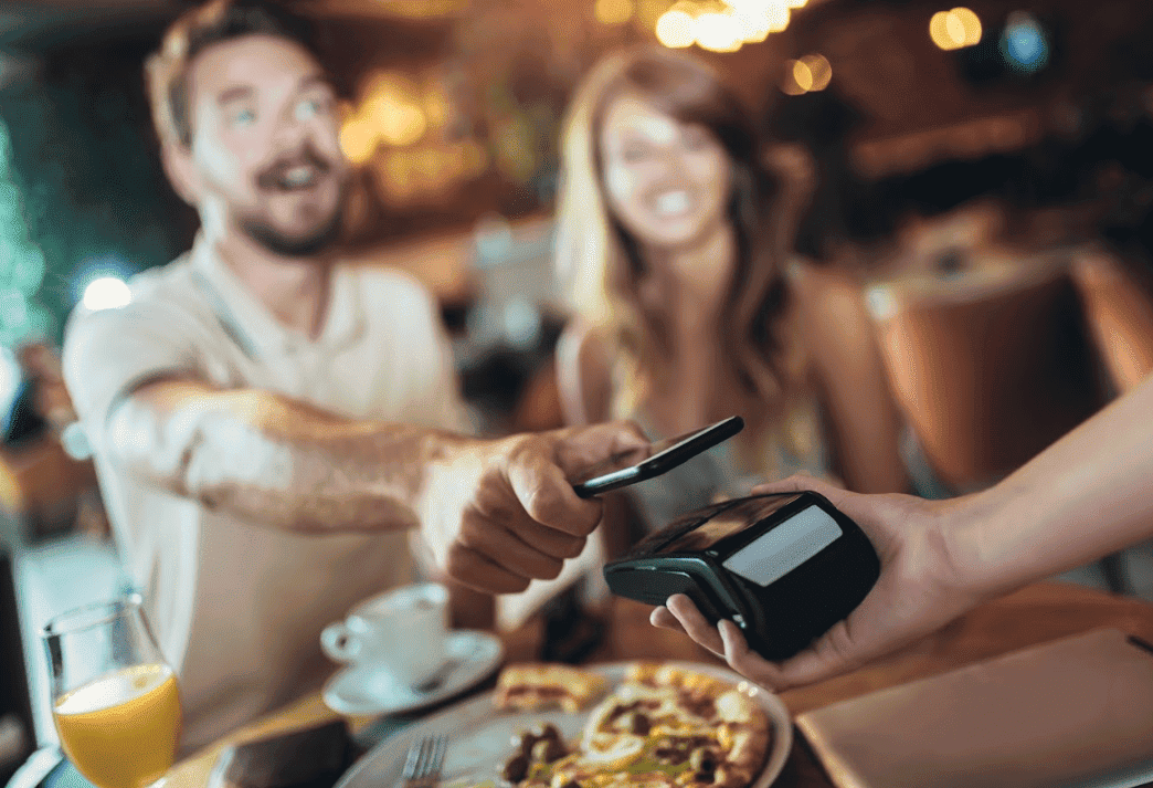 Ein Mann bezahlt in einem Restaurant per kontaktloser Smartphone-Zahlung an einem Kassenterminal.